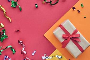 Weihnachtskomposition. Geschenkbox mit rotem Band und Konfetti-Dekorationen auf buntem Hintergrund aus Pastellpapier. Weihnachten, Winter, Neujahrsfeierkonzept. flach legen, Ansicht von oben, Platz kopieren foto