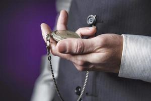 Mann im eleganten Anzug auf violettem Hintergrund, der die Zeit in seiner Taschenuhr liest foto