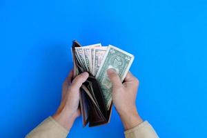 Finanzen und Bankwesen werden durch eine Hand dargestellt, die eine Banknote mit dem Konzept des Geldes auf blauem Hintergrund hält.