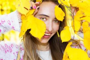 Porträt eines schönen Mädchens, das ihr Gesicht hinter den Herbstblättern versteckt, Nahaufnahme foto