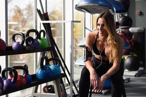junge Frau hört Musik mit Smartphone im Fitnessstudio sitzen