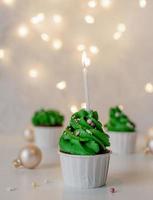 weihnachtsbaumförmige Cupcakes, umgeben von festlichen Dekorationen und Lichtern im Hintergrund