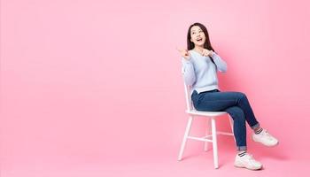 Porträt des schönen asiatischen Mädchens, das im Stuhl sitzt, lokalisiert auf rosa Hintergrund foto