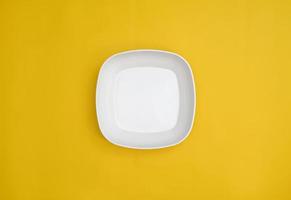 leere weiße quadratische Platte auf gelbem Hintergrund isoliert. ein weißer Teller von oben. ein quadratischer Teller mit abgerundeten Ecken.