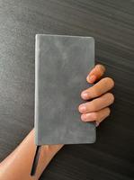 Notizbuch in der Hand. ein kleines graues Notizbuch, um alles festzuhalten, auch Ideen und wesentliche Dinge. geschlossenes Notizbuch mit Trennwand.