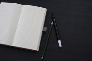 schwarzer Schreibtisch mit Notizbuch und Bleistift darauf. ein Notebook-Modell auf dem Schreibtisch als Arbeitsplatzlayout. Büroobjekt auf schwarzem Hintergrund isoliert. foto