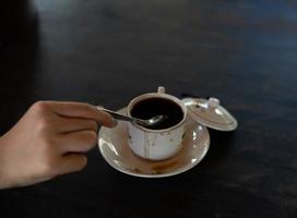 Auf dem Tisch steht eine Tasse heißen Kaffee. Ein Mädchen hält ein leckeres Getränk in der Hand. eine Art Freizeitvergnügen.