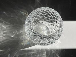 Luxuriöses Bonbonglas aus Kristall, das mit Sonnenlicht übergossen wird und Schatten reflektiert. ein einzelner transparenter Glasbehälter für minimalistische Heimdekoration. foto