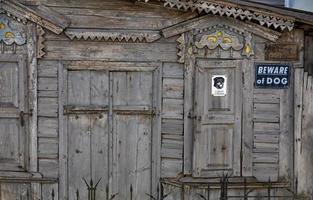 Teil der Holzfassade eines alten baufälligen Hauses mit geschnitzten Platten, geschweiften Wandelementen und Metallstangen mit einem Hundeschild. foto