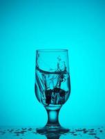 ein Eiswürfel fällt in ein Glasglas mit Wasser foto