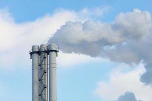 Rauch- und Dampfemissionen aus einem Industrieschornstein in einen klaren Himmel. foto