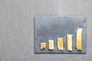 Pfannkuchen mit Hüttenkäse auf grauem Schiefer sind in Form eines wachsenden Trends auf dunklem Betonhintergrund angeordnet.