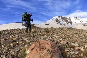 Tourist erklimmt den felsigen Hang des Berges zum schneebedeckten Gipfel foto
