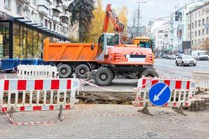 Schwere Straßenmaschinen, ein Bagger und ein Lastwagen auf einem eingezäunten Abschnitt eines Bürgersteigs der Stadt sind an der Reparatur einer Heizungsleitung beteiligt. foto