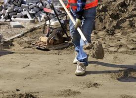 Verlegung von Fliesen auf dem Gehweg, ein Arbeiter trägt eine Bauschaufel Sand um das Fundament zu nivellieren, Nahaufnahme.