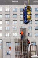 Arbeiter in leuchtend orangefarbenen Westen und Schutzhelmen montieren die Schalung auf einem Metallrahmen aus Stahlarmierung. foto