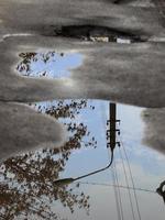Reflexion des Himmels, die Silhouette einer Straßenlaterne und ein Baum in einer Pfütze auf schlechtem Asphalt. foto