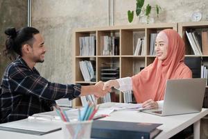 Startup-Geschäftsleute, die islamische Menschen sind, schütteln sich die Hände, um sich mit Handelspartnerschaften zu befassen und zusammenzuarbeiten, nachdem ein junger männlicher Mitarbeiter in dem kleinen Casual-Büro ein Erfolgsdiagramm präsentiert hat. foto