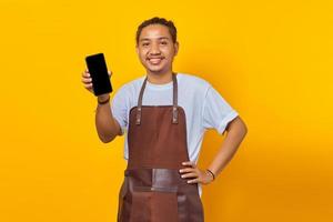 Aufgeregter asiatischer Barista, der einen leeren Bildschirm des Smartphones über gelbem Hintergrund zeigt foto