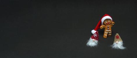 Weihnachtskonzept. Gnome und Lebkuchenmann in Weihnachtsmütze auf schwarzem Hintergrund mit Kopierraum