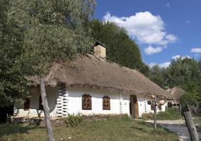 altes traditionelles ukrainisches Landhaus mit Strohdach und Weidenzaun im Garten foto