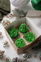 Weihnachtsbaumförmige Cupcakes in handwerklicher Öko-Box, umgeben von festlicher Dekoration