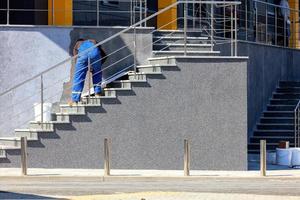 Arbeiter in blauen Overalls bringt dekorativen Fassadenputz an die Wand des Gebäudes. foto