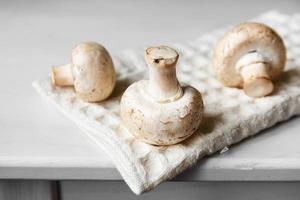 Champignons Champignons auf der Küchenserviette auf einem weißen Holztisch foto