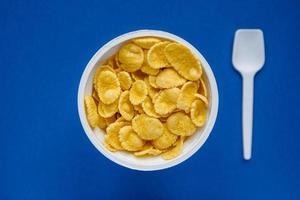 Cornflakes in weißer Schüssel mit Löffel auf blauem Hintergrund foto