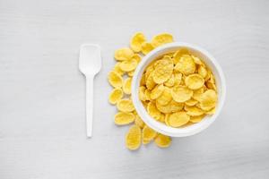 Cornflakes in weißer Schüssel mit Löffel auf weißem Holzuntergrund foto