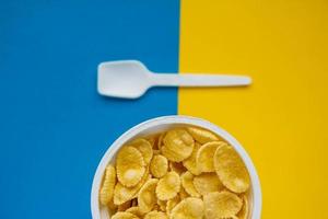 Cornflakes in weißer Schüssel mit Löffel auf blauem und gelbem Hintergrund foto