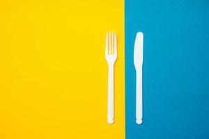 weiße Gabel und Messer aus Kunststoff auf gelbem und blauem Hintergrund. Koch Utensilien foto