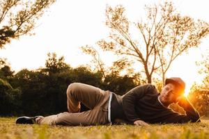 Mann liegt auf dem grünen Gras und genießt einen Sonnenuntergang in einem Park foto