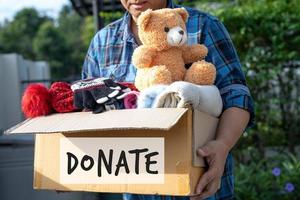 Kleiderspendenbox mit gebrauchter Kleidung und Puppe zu Hause halten, um die Hilfe für arme Menschen in der Welt zu unterstützen. foto