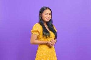 lächelnde junge asiatische frau hält die hand zusammen und fühlt sich optimistisch auf lila hintergrund foto