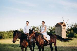 Mädchen in einem weißen Sommerkleid und ein Typ in einem weißen Hemd auf einem Spaziergang mit braunen Pferden foto