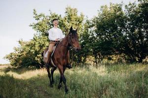 Kerl in einem weißen Hemd auf einem Spaziergang mit braunen Pferden foto