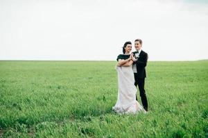 der Bräutigam im braunen Anzug und die Braut im elfenbeinfarbenen Kleid auf grüner Wiese foto