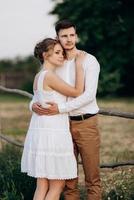 Mädchen in einem weißen Sommerkleid und ein Typ in einem weißen Hemd auf einem Spaziergang bei Sonnenuntergang mit einem Blumenstrauß foto