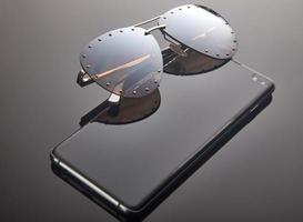 Damensonnenbrille und Smartphone auf grauem Hintergrund mit Farbverlauf mit Reflexion. Platz für Text foto