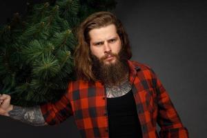 gut aussehender Mann mit langen Haaren, der einen synthetischen Weihnachtsbaum hält foto