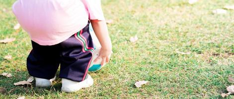 Mädchenhände heben weißen und blauen Fußball auf. Kind beim Sport im Sommer. Kind trägt weiße Turnschuhe. auf grünem Rasen. foto