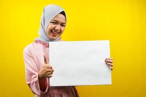 hübsche junge muslimische Frau, die fröhliche leere leere Banner, Plakate, weiße Tafeln, leere Schilder, weiße Werbetafeln hält, etwas im Kopierraum präsentiert, Werbung foto