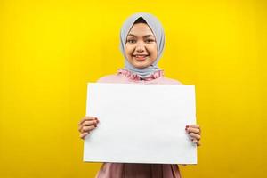 hübsche junge muslimische Frau, die fröhliche leere leere Banner, Plakate, weiße Tafeln, leere Schilder, weiße Werbetafeln hält, etwas im Kopierraum präsentiert, Werbung