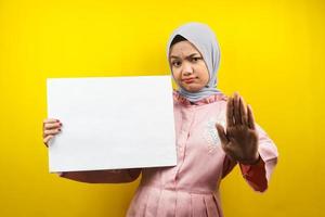Hübsche junge muslimische Frau, die leere leere Banner, Plakate, weiße Tafeln, leere Schilder, weiße Werbetafeln hält und etwas im Kopierraum präsentiert, Werbung