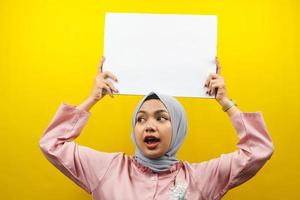 Hübsche junge muslimische Frau, die leere leere Banner, Plakate, weiße Tafeln, leere Schilder, weiße Werbetafeln hält und etwas im Kopierraum präsentiert, Werbung foto