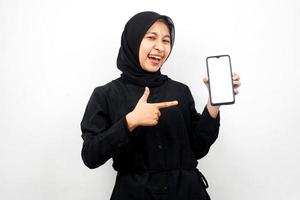 schöne junge asiatische muslimische frau schockiert, überrascht, wow-ausdruck, hand hält smartphone mit weißem oder leerem bildschirm, fördert app, fördert produkt, präsentiert etwas, isoliert foto