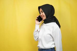 Schöne junge asiatische muslimische Frau, die selbstbewusst und fröhlich lächelt und jemanden anruft, mit Blick auf leeren Raum, isoliert auf gelbem Hintergrund, Werbekonzept foto