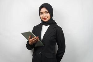 schöne junge asiatische muslimische Geschäftsfrau zuversichtlich und lächelnd, mit den Händen, die Tablette halten, Zeit zum Arbeiten, produktive Zeit, isoliert auf grauem Hintergrund foto