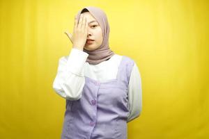 schöne asiatische junge muslimische frau mit der hand, die ein auge bedeckt und in die kamera schaut, die auf gelbem hintergrund isoliert ist
